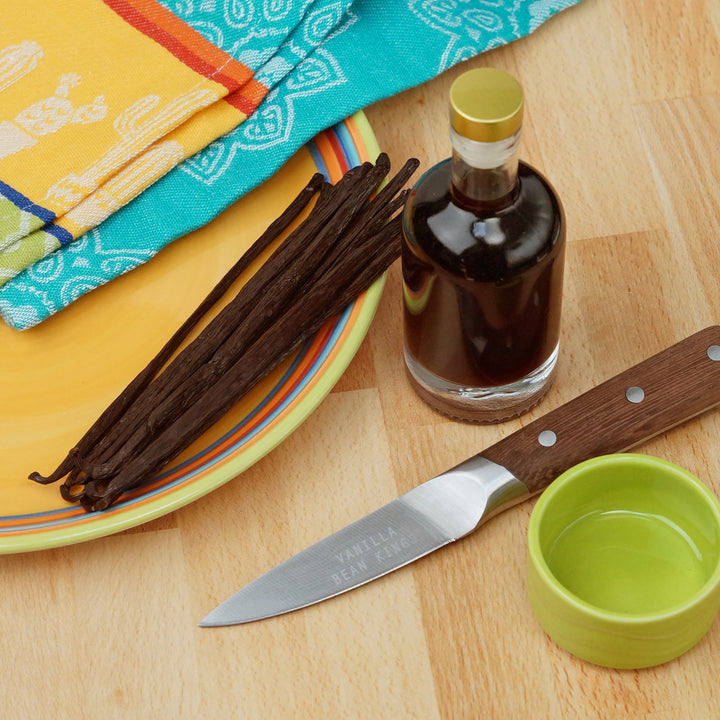 mexican grade b vanilla beans on a plate next to a bottle of vanilla extract placed by a dish and a knife