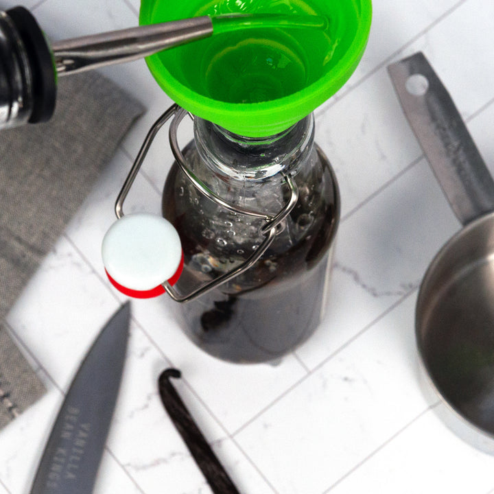 sri lanka vanilla beans in glass jar showing liquid being poured into glass with a funnel