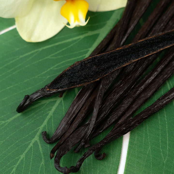 vanilla beans on green leaf with 1 split showing caviar